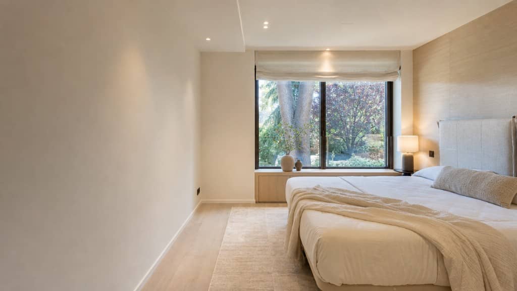 Dormitorio principal de chalet con panelado de madera y vistas al jardín