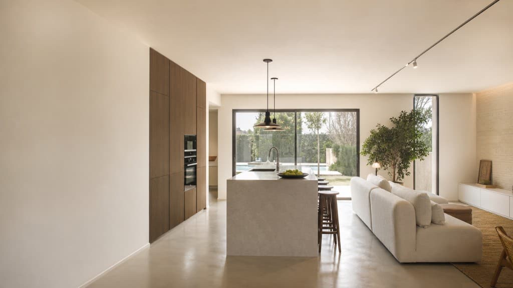 Cocina con isla abierta a zona de día y vistas a jardín con piscina en chalet